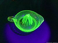 Uranium glass citrus juicer glowing bright green under UV light, showing the ribbed bowl and pointed juice extractor cone.