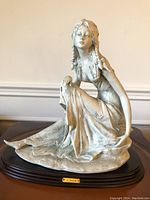 Front view of porcelain biscuit woman sculpture seated on wood base with braided hair and flowing dress, signature plate visible
