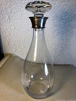 Full view of the clear crystal decanter with a broad base, narrow neck, and a sterling silver mounted collar topped with a crystal stopper.