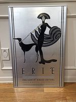 Framed Erte poster titled 'Woman And Dog' with silver background and black decorative figure, shown full front view.