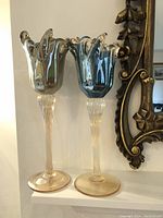 Two tall Murano Italian art glass candle holders shown side by side with fluted tulip-shaped tops and clear twisted stems with beige tinted bases.