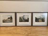 Three framed aquatint prints displayed side by side on floor against a white wall