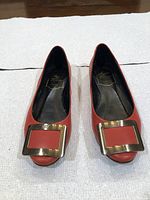 Top view of pair of red Roger Vivier women’s shoes, showcasing gold-tone square buckles and peep-toe design