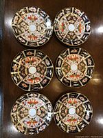 Top-down view of 6 Royal Crown Derby Imari dishes arranged in two rows of three, showing intricate multi-colored floral and geometric patterns with gold accents.