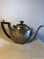 Full view of teapot showing fluted lower body, hinged lid, finial and black handle