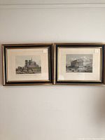 Two framed steel engravings on a wall showing views of Paris landmarks, one featuring Notre Dame Cathedral and one a temple-like building.