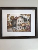 Framed watercolor painting showing an autumn scene with a mill building beside water, set in a wooded area, with a fence visible on one side.