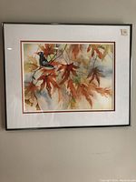 Framed watercolor painting showing a naturalistic scene with bird and colored leaves in fall palette.