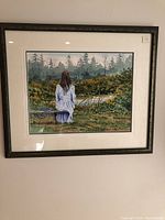 Framed watercolor painting showing a woman in white sitting on a bench in a natural outdoor setting with trees and greenery.