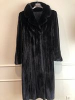 Front view of full-length black mink fur coat on hanger against white wall