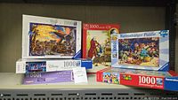 Lot displayed on a shelf showing six puzzle boxes stacked including Disney Lion King, Super Mario, Mozart with CD, Toy Story 100-piece puzzle
