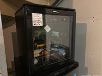 Front and side view of the Danby 16 bottle wine cooler showing the glass door with wine bottles inside and black body.