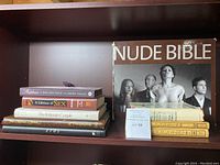 Books arranged on a bookshelf showing titles Nude Bible, Erotica by Anais Nin, Eros, and others