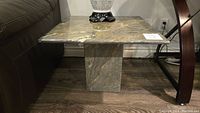 Full side view of green marble side table showing base and top surface next to sofa.