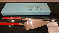Cake serving knife and server with red and pink enamel handles placed in front of a Kate Spade New York blue box
