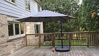 Grey 10' diameter cantilever umbrella open on wooden deck with weighted base and crank arm