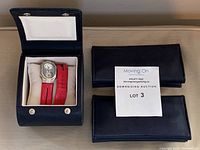 Watch on pillow inside open black leather box with two black pouches and lot tag