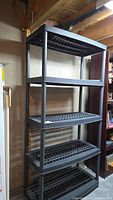 Full view of the black plastic resin shelving unit showing five ventilated shelves supported by four cylindrical legs.
