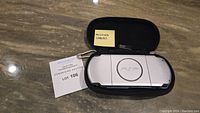 Sony PSP portable console resting on a marble surface inside an open zippered black travel case bearing a note 'MISSING CABLES'.