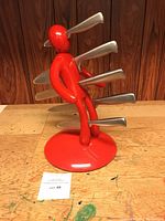 Red plastic human-shaped knife block holding 5 knives shown from side on wooden surface.