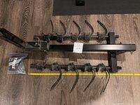 Top-down view of the assembled bike rack showing five adjustable rubber straps and the hitch frame laid on a wood floor with a tape measure for scale.