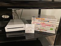 White Wii console on stand next to stack of eight game cases