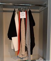 Lot of sweaters hanging on a closet rack showing six unitary sweaters of various colors and fabrics.