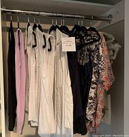 Full view of the lot of women's tops hanging in closet, showing white sleeveless blouses and patterned short-sleeved blouses