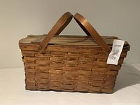 Photo of an antique woven wooden picnic basket with two handles and a hinged wooden lid.