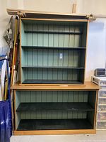Front view of the two-piece wooden bookcase showing three upper green shelves and two lower black shelves with wooden top, crown molding placed on top.