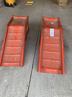 Top-down view of two orange metal ramps placed side by side on a concrete floor, showing surface wear and rust.