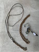 Photo showing a manual come-a-long lever hoist with attached chain and hook, placed on concrete alongside a longer rusty steel chain.