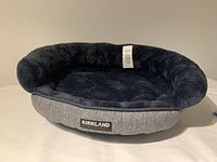 Photo showing Kirkland Signature dog bed, size 18, gray fabric exterior and plush black interior, laid out flat.