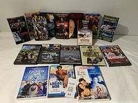 Photo of a collection of 9 VHS tapes standing upright and 8 DVDs lying flat, showing covers and titles.