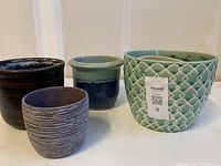 Four assorted flower pots in an indoor setting on white surface and beige wall background.