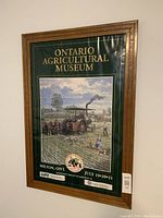 Framed Ontario Agricultural Museum poster showing vintage steam tractor in a field with workers, housed in decorative wooden frame without glass