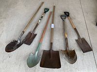 Six garden shovels arranged on concrete floor showing different blade shapes and wooden handles.