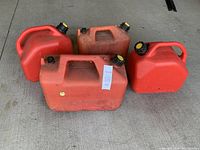 Four used red plastic gas cans arranged on concrete, showing various shapes and sizes with black caps and handles