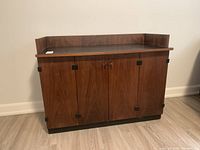 Photo showing front view of midcentury modern wooden cabinet with four doors and black square metal accents on hinges.