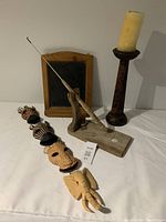 Wide shot of lot contents showing fishing pole with stand, chalkboard, tall candleholder with candle and connected animal masks arranged on white surface.