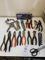 Photo of diverse pliers and hand tools spread on a white surface, including locking pliers, snap ring pliers, wire cutters, scissors, and a boxed Mastercraft snap ring plier set.