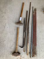Photo shows two wooden-handled sledgehammers, three metal pry bars of different lengths and shapes, and six metal rebar stakes with rust.
