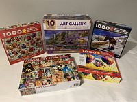 Photo showing five 1000-piece Art Gallery puzzles arranged on a flat surface, showcasing puzzle box artwork and branding.