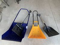 Photo showing 4 snow shovels, 2 large scoop shovels in blue and yellow, and 2 smaller black shovels with different handles.