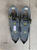 Photo showing pair of gray snowshoes with black and yellow bindings laid on concrete floor, labeled with lot tag 63.