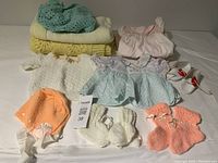 Various vintage baby clothes and blankets including knitted items and dresses laid out on a flat surface.