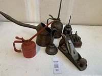Overview photo showing four vintage oil cans, a metal hand plane and wooden block with assorted driver bits.