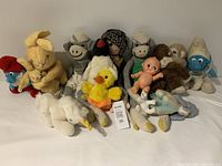 Overall view of the vintage 1970s plush toys including two Smurfs, various animals, and a small doll.