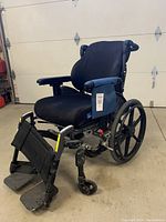 Side and front angle of black manual wheelchair showing memory foam seat cushion, padded armrests, adjustable footrests, and large rear wheels.