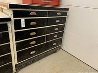 Front view of black metal workshop storage bench with multiple drawers, showing metal handles and some wear.